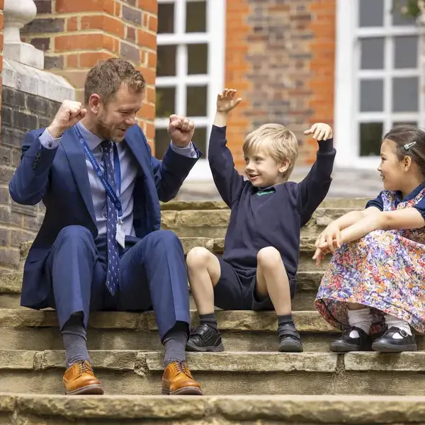 Prep pupils sitting on the stairs with the teacher of Ibstock Place School, a private school near Richmond, where wellbeing and pastoral care is at the heart of what we do.