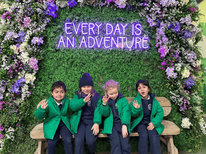 Pre-prep pupils sitting a bench which is decorated with flowers.